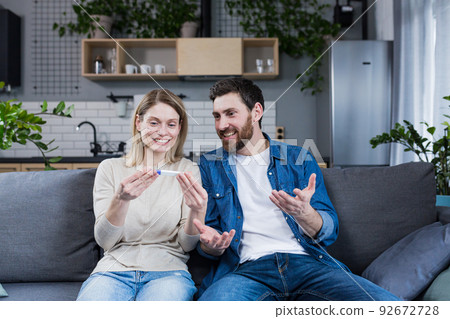 Happy couple man and woman on the couch sitting and rejoicing in a positive pregnancy test Happy couple man and woman on the couch sitting and rejoicing in a positive pregnancy test 92672728