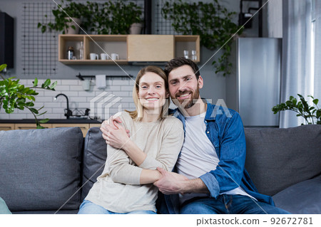 Young married couple man and woman sitting together on sofa and hugging, portrait of middle aged family looking at camera 92672781