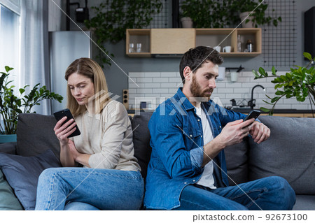 Conflict, quarrel. Man and woman, couple, family sitting on the couch with their backs to each other with phones, do not talk to each other, do not pay attention, busy with phones 92673100