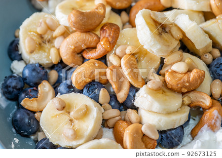 Beautiful breakfast - cottage cheese, berries cashew, cedar, blueberry and honey in the plate. Good morning. 92673125