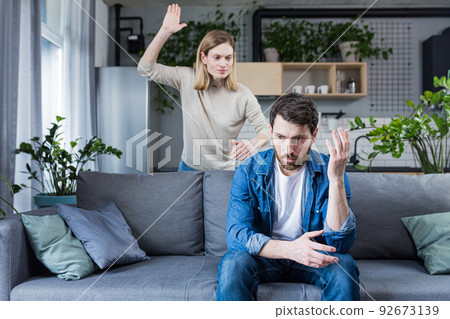 Family quarrel, woman quarrels and yells at the loser's husband, couple at home sitting in the living room on the couch Family quarrel, woman quarrels and yells at the loser's husband, couple at home sitting in the living room on the couch 92673139