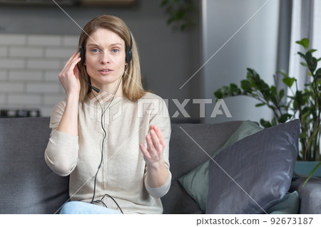 A woman at home uses a headset for a video call, looks at the camera and smiles A woman at home uses a headset for a video call, looks at the camera and smiles 92673187