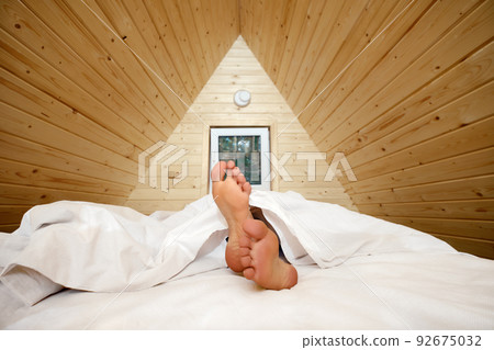 Legs of woman stick out from under the blanket Legs of woman stick out from under the blanket 92675032