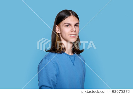 Headshot portrait of teenage guy looking at camera on blue background Headshot portrait of teenage guy looking at camera on blue background 92675273