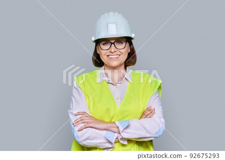 Portrait of female industrial worker in protective hard hat vest on gray background 92675293
