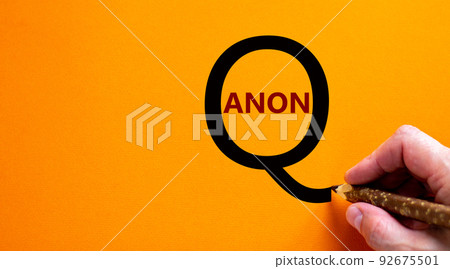Q Anon symbol. Hand writing words 'Q Anon', isolated on beautiful orange background. Business and q Anon concept, copy space. 92675501