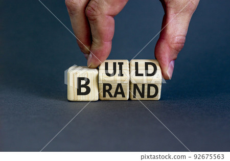 Build your brand symbol. Concept words Build brand on wooden cubes. Businessman hand. Beautiful grey table grey background. Build your brand and business concept. Copy space. 92675563