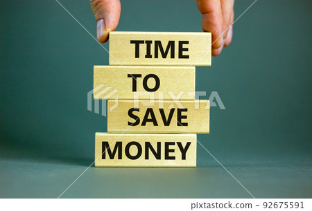 Time to save money symbol. Concept words Time to save money on wooden blocks on a beautiful grey table grey background. Businessman hand. Business, finacial and time to save money concept. Time to save money symbol. Concept words Time to save money on wooden blocks on a beautiful grey table grey background. Businessman hand. Business, finacial and time to save money concept. 92675591