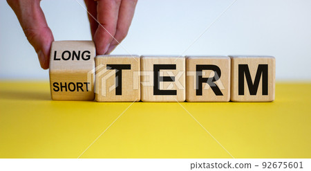 Hand turns a cubes and changes the expression 'SHORT TERM' to 'LONG TERM' or vice versa. Beautiful yellow background. Business concept, copy space. 92675601