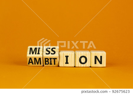 Do your mission with ambition. Turned wooden cubes and changed the word mission to ambition. Beautiful orange table, orange background, copy space. Business, mission or ambition concept. 92675623
