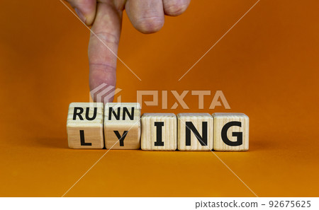 Lying or running. Hand is turning cubes and changes the word 'lying' to 'running'. Beautiful orange background. Lifestyle and motivational concept, copy space. 92675625