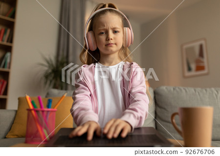Displeased Schoolgirl Using Laptop Wearing Headphones Learning Online At Home 92676706