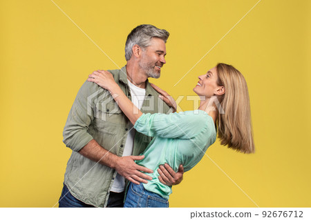 Loving middle aged woman and her husband dancing and having fun on yellow studio background Loving middle aged woman and her husband dancing and having fun on yellow studio background 92676712