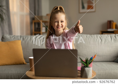 Schoolgirl Using Laptop Gesturing Thumbs Up Approving E-Learning At Home 92676762