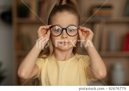 Portrait Of Little Girl Wearing Eyeglasses Sitting In Library Portrait Of Little Girl Wearing Eyeglasses Sitting In Library 92676779