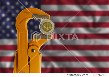 Ethiopian one Birr coin held in an orange plumber wrench on the background of the flag of the United States. reverse of the coin. 92676786