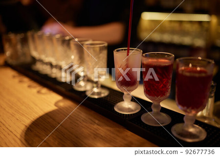 Bartender pouring strong alcoholic drink into small glasses on bar, shots. Bartender pouring strong alcoholic drink into small glasses on bar, shots. 92677736