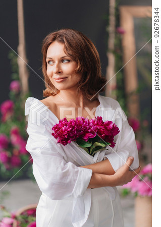 a beautiful middle-aged woman in white clothes with a bouquet of peonies. a beautiful middle-aged woman in white clothes with a bouquet of peonies. 92678344