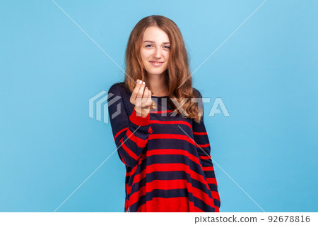 Give me money, many dollars. Smiling woman wearing sweater showing money gesture, hinting at salary increase, having business idea to earn income. Indoor studio shot isolated on blue background. 92678816