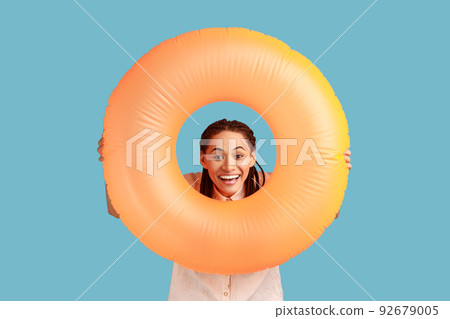 Lovely cheerful woman with dreadlocks looks through swimming hole, has excited toothy smile, spends summer holidays on beach, enjoys awesome vacation. Indoor studio shot isolated on blue background. 92679005