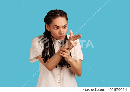 Portrait of woman with black dreadlocks pointing finger gun, aiming and threatening to shoot with pistol hand gesture, wearing white shirt. Indoor studio shot isolated on blue background. 92679014