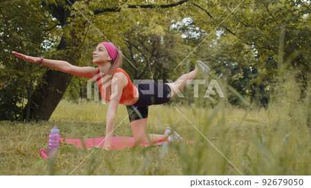 Athletic sporty fit girl doing workout in park on sport mat performing training yoga, plank pose 92679050