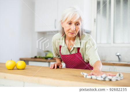 Mature woman cleaning kitchen table at home Mature woman cleaning kitchen table at home 92682235