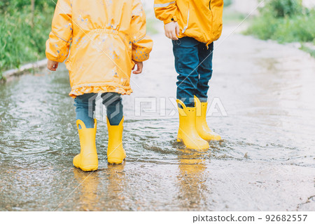 Children in yellow rubber boots walk through puddles Children in yellow rubber boots walk through puddles 92682557