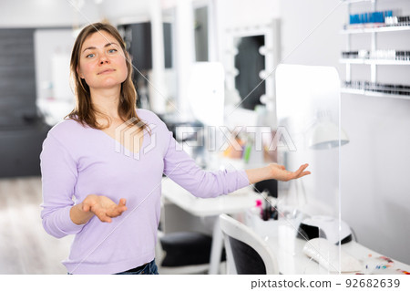 Smiling professional female manicurist inviting to nail salon Smiling professional female manicurist inviting to nail salon 92682639