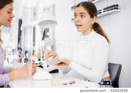 Young female manicurist showing palette of nail varnishes to woman client Young female manicurist showing palette of nail varnishes to woman client 92682646