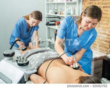 Two masseuses give the female client a massage with a devices 92682702