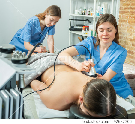 Cosmetologists performing hardware body procedure for young woman Cosmetologists performing hardware body procedure for young woman 92682706