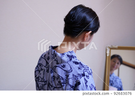 Back view of a woman wearing an indigo dyed yukata and looking in the mirror Back view of a woman wearing an indigo dyed yukata and looking in the mirror 92683076