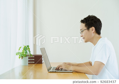 Happy Asian young businessman in relax casual style doing a video conference with his colleague, using online meeting and video conference for avoiding COVID-19 pandemic. New normal lifestyles. Happy Asian young businessman in relax casual style doing a video conference with his colleague, using online meeting and video conference for avoiding COVID-19 pandemic. New normal lifestyles. 92683437