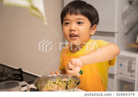 A 4-year-old boy who mixes ingredients in a bowl with his mother's help 92684374