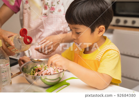 A 4-year-old boy who mixes the ingredients in the bowl with his mother and adds soy sauce for seasoning. A 4-year-old boy who mixes the ingredients in the bowl with his mother and adds soy sauce for seasoning. 92684380