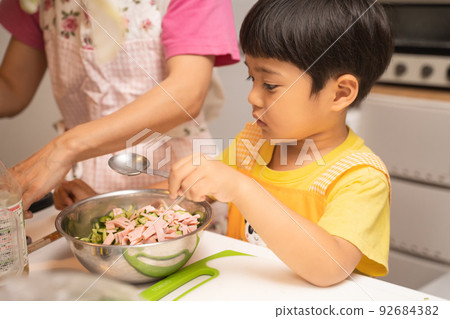 一個 4 歲的男孩在和他的母親一起將碗裡的材料混合後，試圖加入醬油調味。 92684382