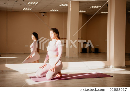 Young sporty woman, fitness instructor in pink sportswear doing stretching and pilates on yoga mat in the studio with mirror. Female fitness yoga routine concept. Healthy lifestyle and harmony. Young sporty woman, fitness instructor in pink sportswear doing stretching and pilates on yoga mat in the studio with mirror. Female fitness yoga routine concept. Healthy lifestyle and harmony. 92688917