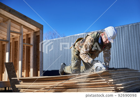 Carpenter using circular saw for cutting wooden OSB board. Man worker building wooden frame house. Carpentry concept. 92690098