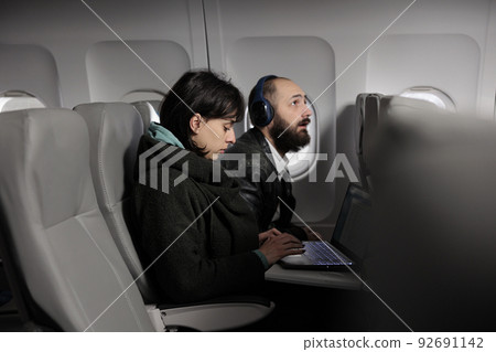 Woman working on laptop during airplane flight abroad, using online internet on computer to travel to holiday destination. Tourist waiting to arrive after commercial flight transportation trip. Woman working on laptop during airplane flight abroad, using online internet on computer to travel to holiday destination. Tourist waiting to arrive after commercial flight transportation trip. 92691142