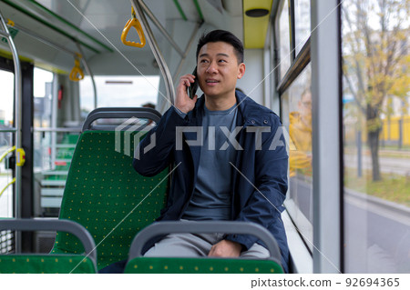 asian man in public bus passenger having fun talking on mobile phone, in casual clothes asian man in public bus passenger having fun talking on mobile phone, in casual clothes 92694365