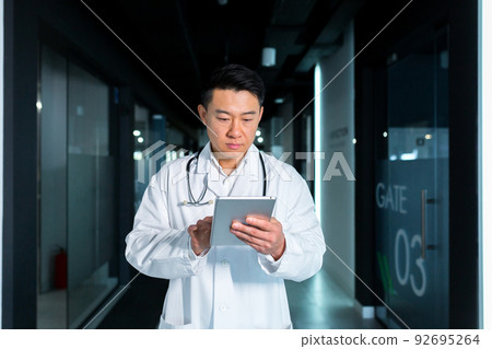 Serious Asian doctor, uses a tablet computer, the man works in a modern clinic 92695264