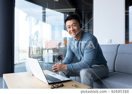 portrait of happy asian call center worker, man smiling and happy working with headset and computer, remote work, video call, online help portrait of happy asian call center worker, man smiling and happy working with headset and computer, remote work, video call, online help 92695388