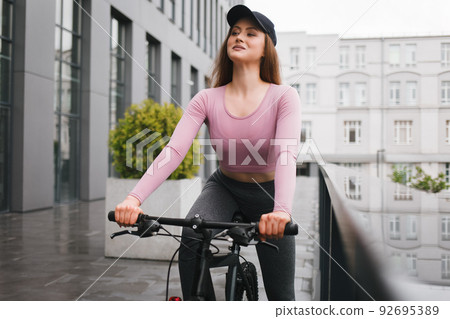 Sporty young woman rides a bicycle on a city alley. Sporty young woman rides a bicycle on a city alley. 92695389