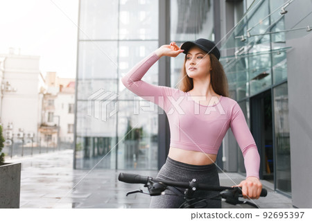 Beautiful girl in cap on a bicycle in the background of a glass building. Beautiful girl in cap on a bicycle in the background of a glass building. 92695397