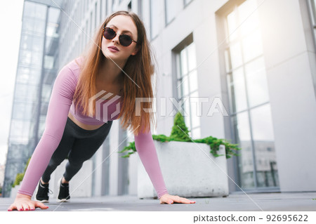 Girl shakes abdominals standing in plank outdoor. 92695622