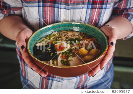 Asian style soup with noodles, egg in bowl in the hands of young woman 92695977
