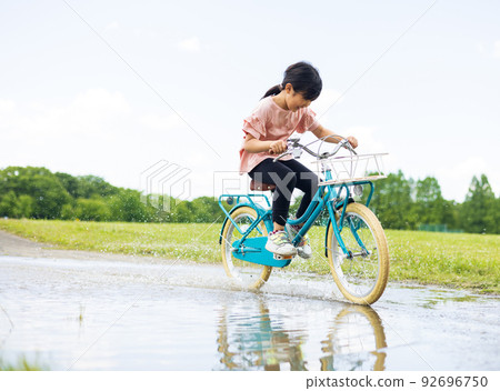 A puddle road A girl riding a bicycle A puddle road A girl riding a bicycle 92696750
