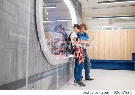 Two friends standing near the window in a modern school Two friends standing near the window in a modern school 92697523
