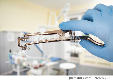 Dentist's hand in glove with rubber dam clamp forceps and clamp. Dentist's hand in glove with rubber dam clamp forceps and clamp. 92697798